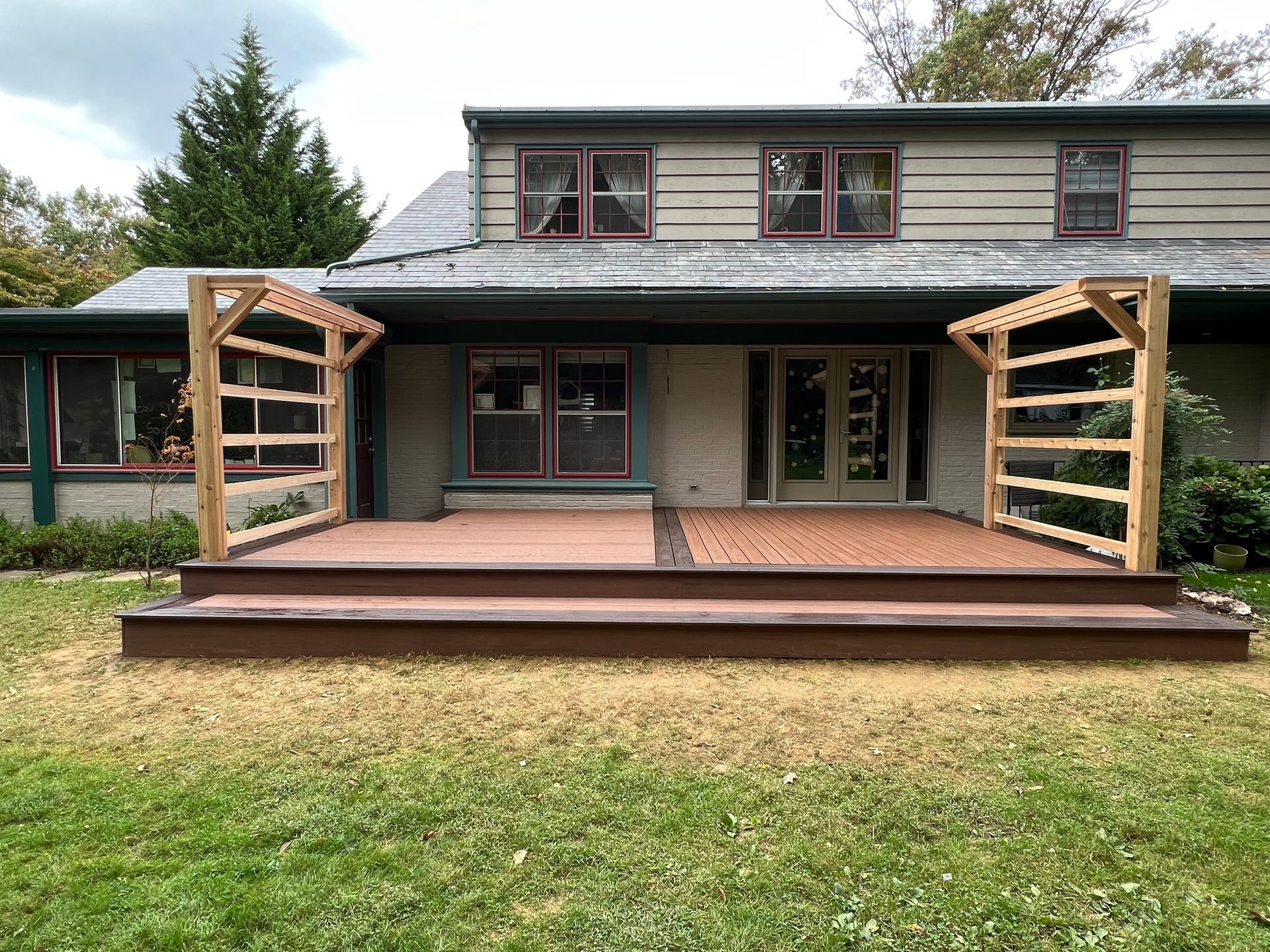 A house exterior featuring a two-level deck with wooden trellises on either side and a grassy yard in the foreground.