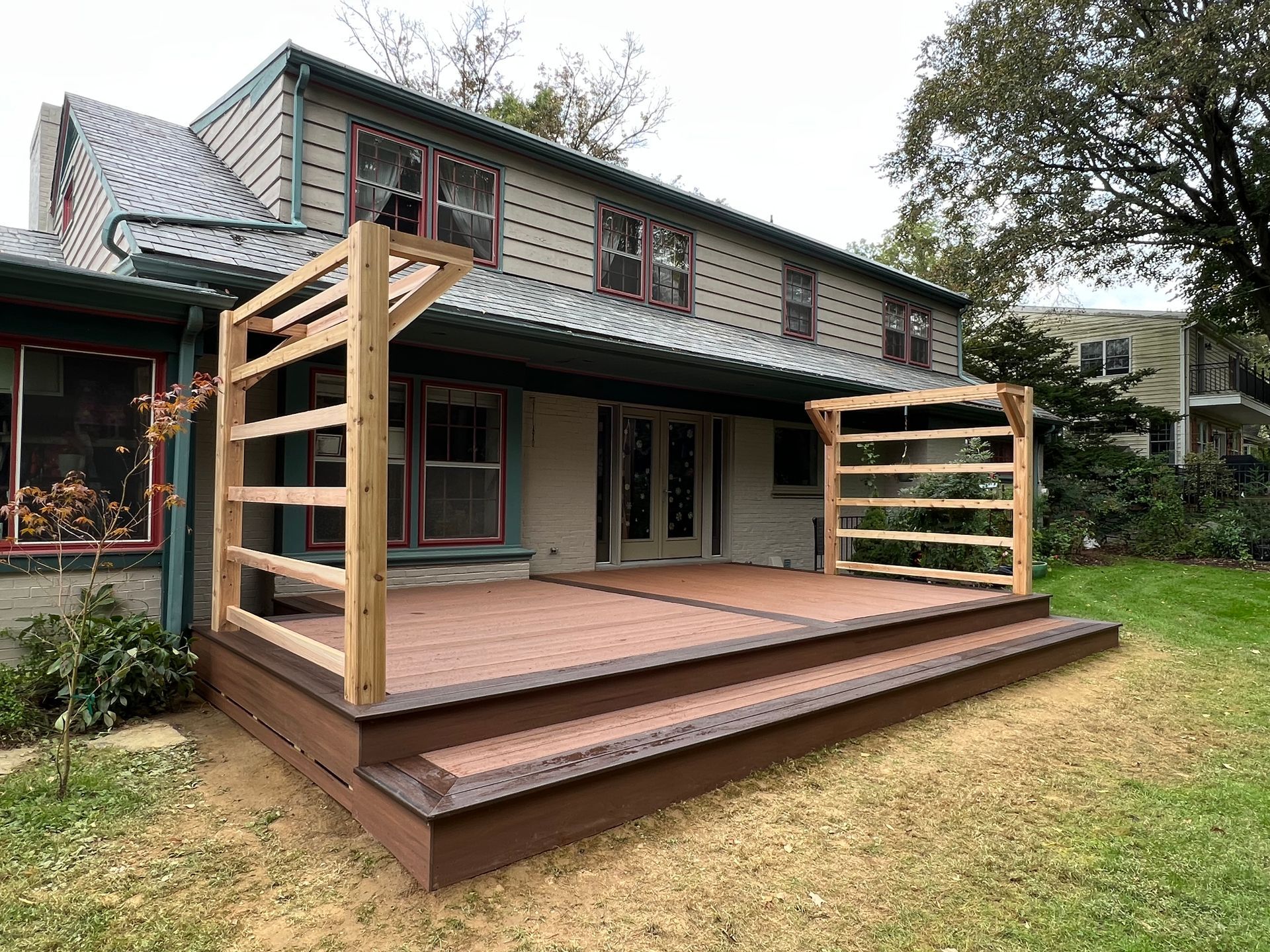 A tan deck featuring a hot tub with a brown cover sits beside a multi-story house with beige siding and blue shutters.