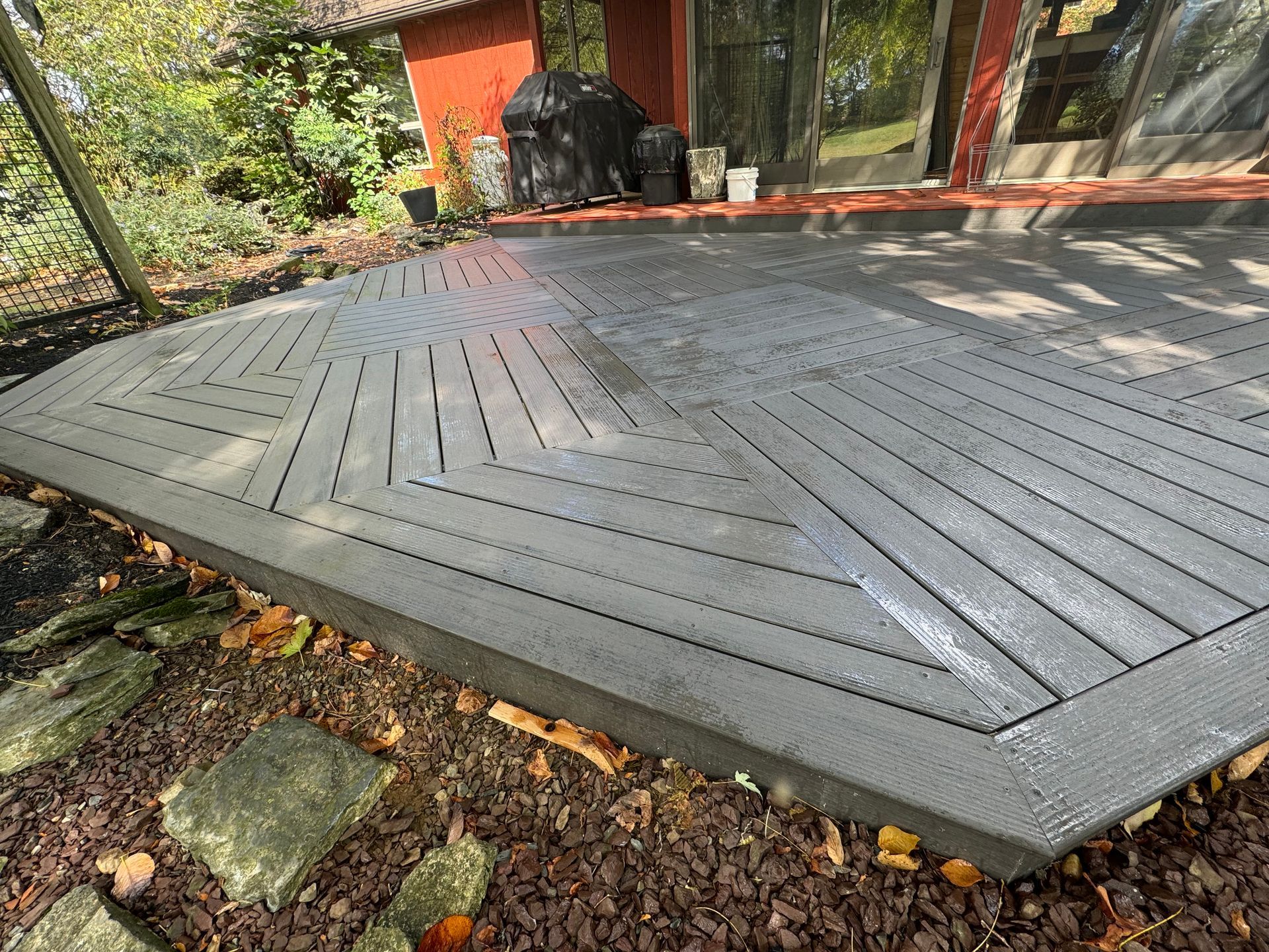 Gray composite deck featuring a geometric inlay pattern, built outdoors next to a home with a red-painted wall.