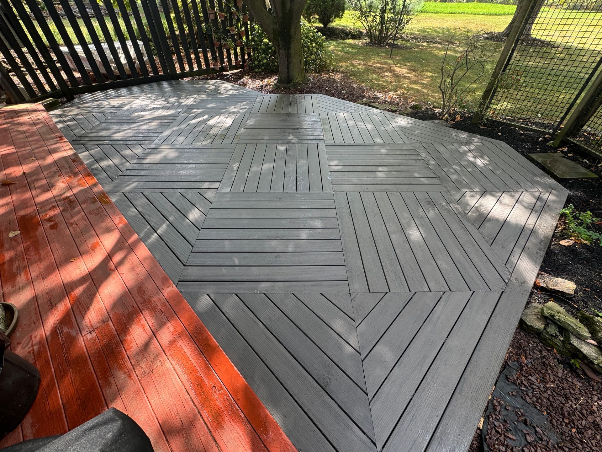 A two-tone deck transition: a reddish-brown wood surface meets a grey, geometrically patterned composite deck area.