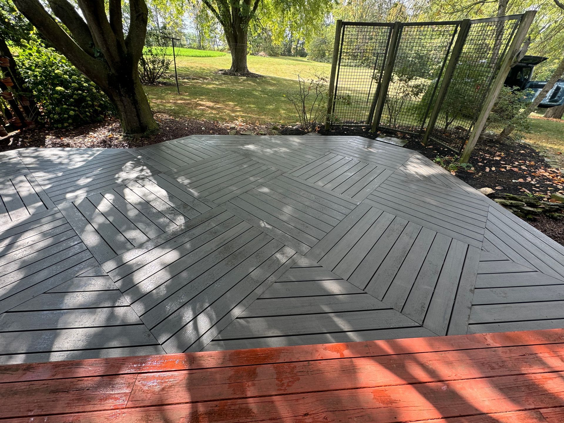 A backyard deck with sections of gray composite decking laid in a geometric herringbone pattern beside orange wood planks.