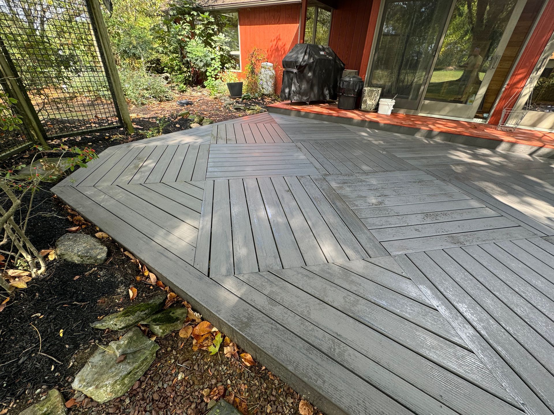 A multi-toned grey composite deck with a geometric herringbone pattern, built off the back of a red house.