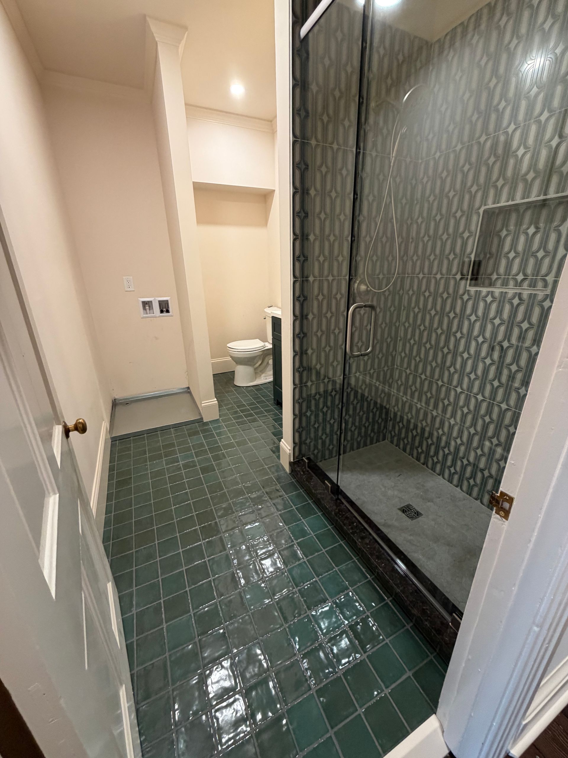 A bathroom with dark green square floor tiles, a glass-enclosed shower with patterned tile walls, and a white toilet.