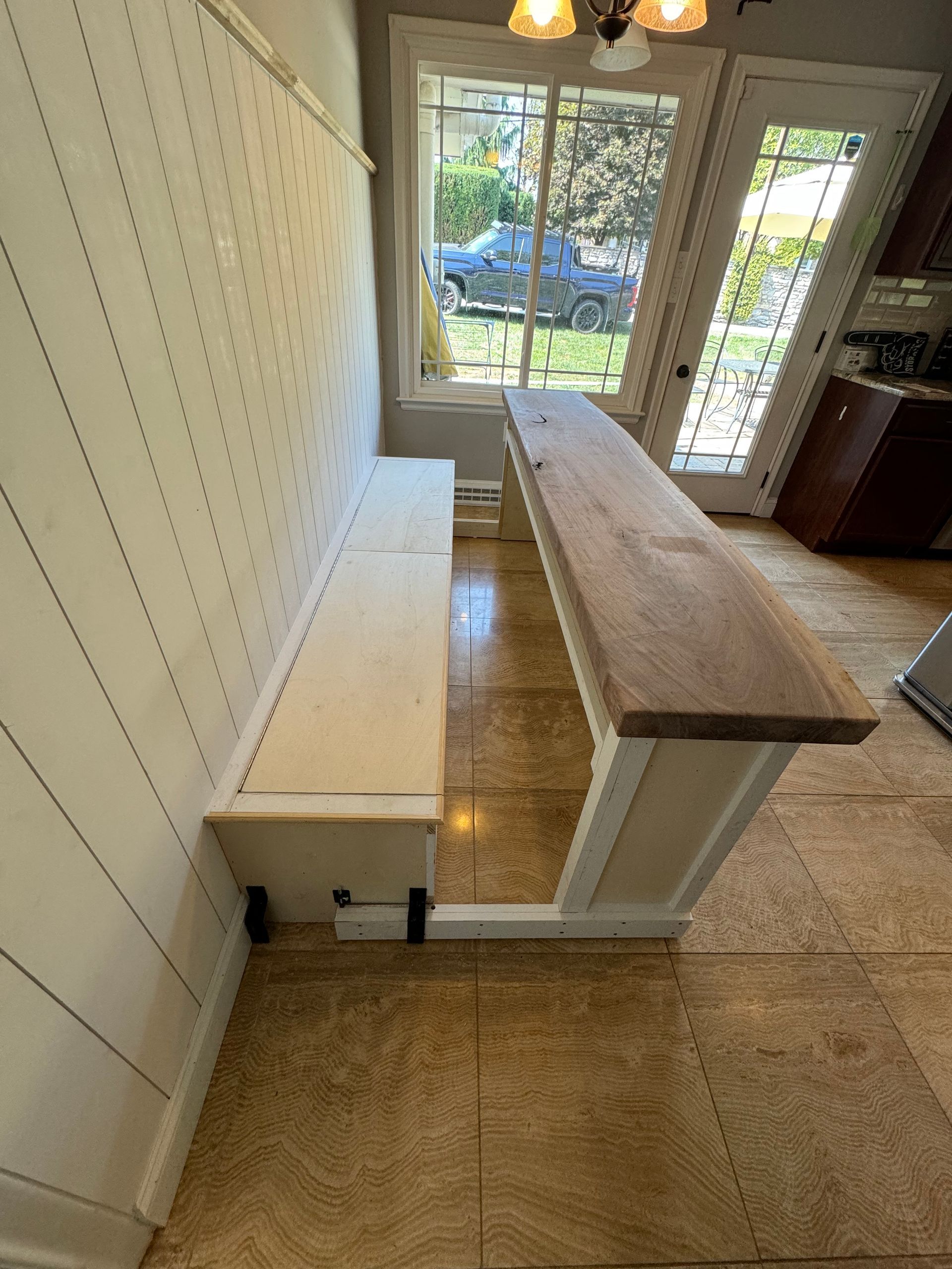 A built-in white bench seat sits against a shiplap wall facing a long, light-wood dining table in a bright room.