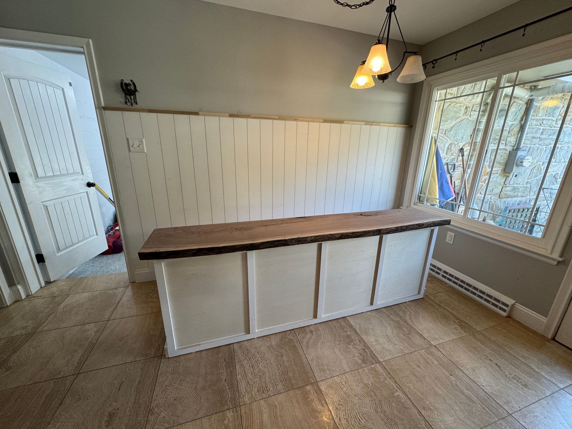A long, wooden-topped kitchen island with white paneled cabinets stands in a room with light grey walls and tiled floors.