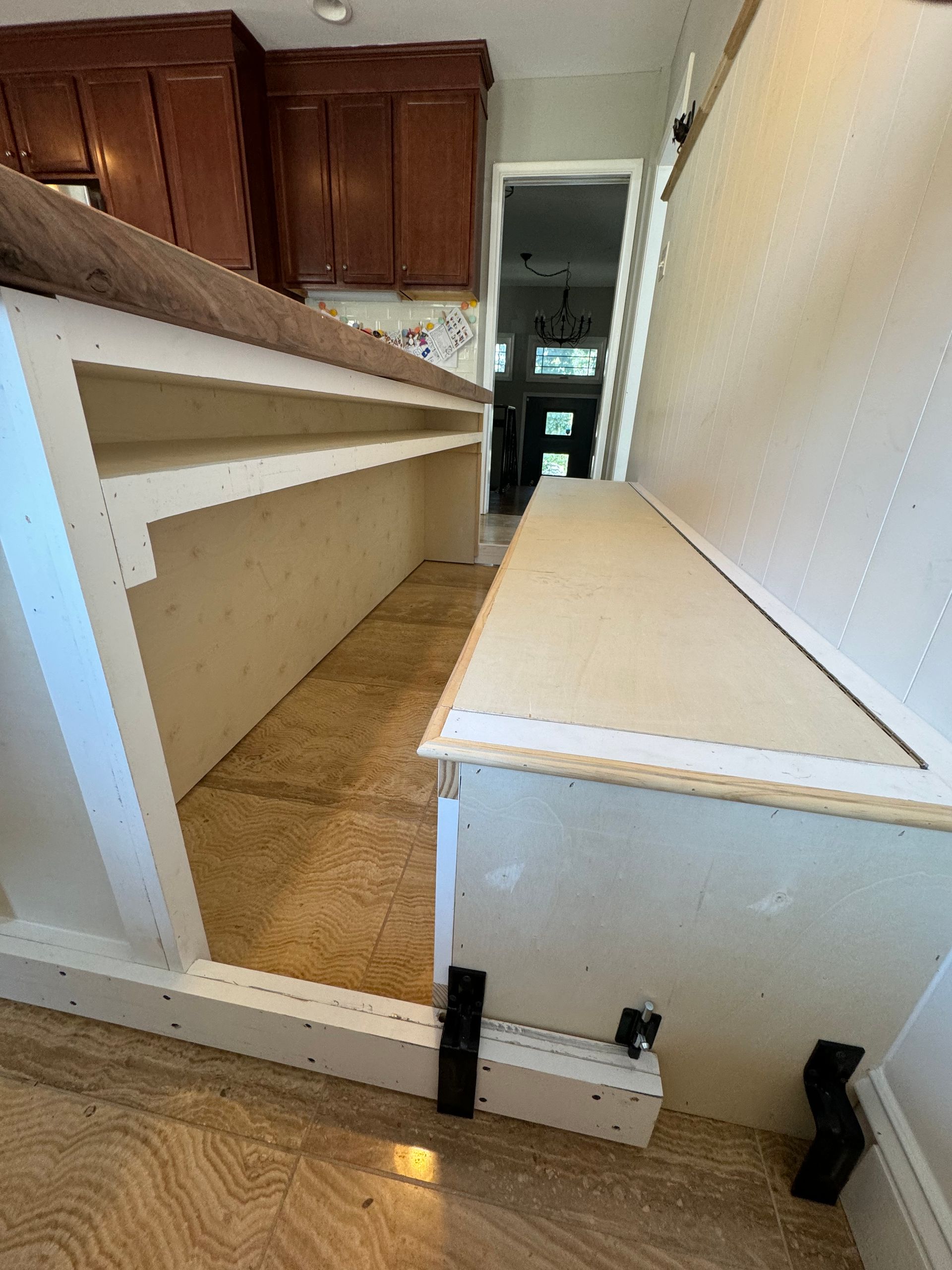 A kitchen island under construction featuring white base cabinets, a wooden countertop, and a newly built bench seat.