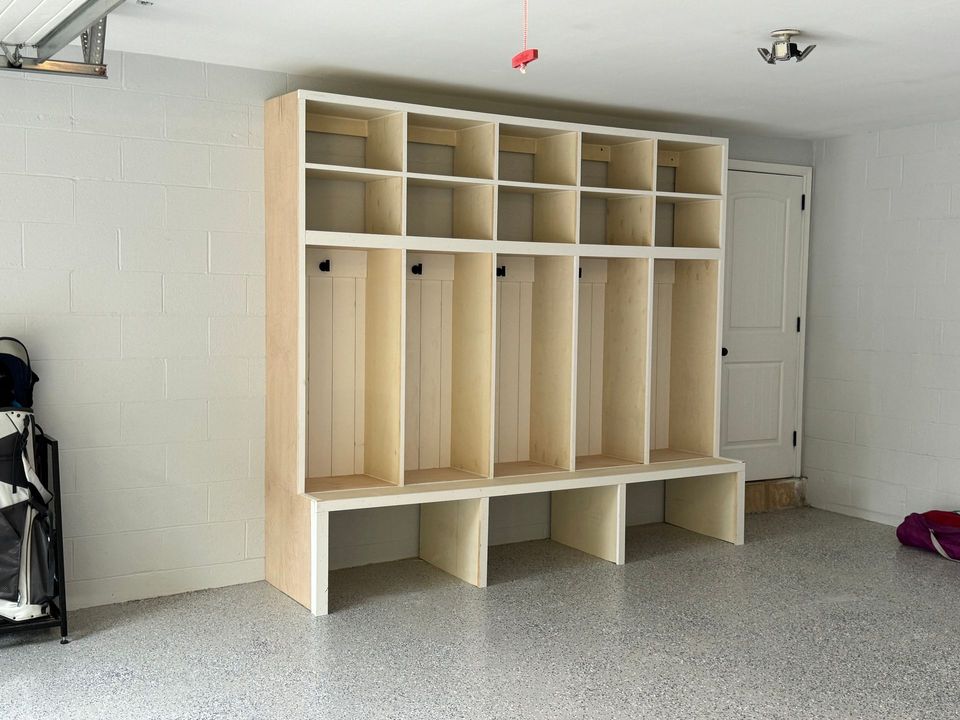 A large, unfinished wooden locker unit with five cubby sections and a bench seat against a garage wall.
