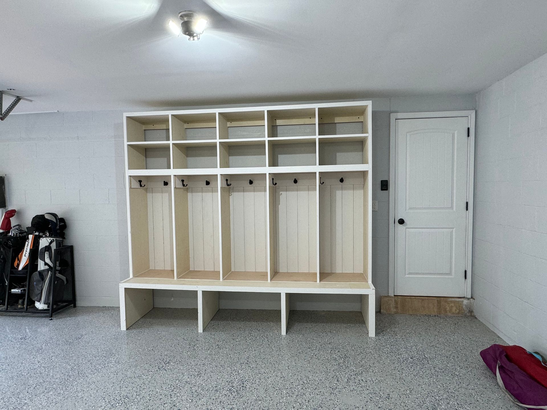 A large, white, five-section wooden mudroom locker unit with shelving and coat hooks installed in a garage.