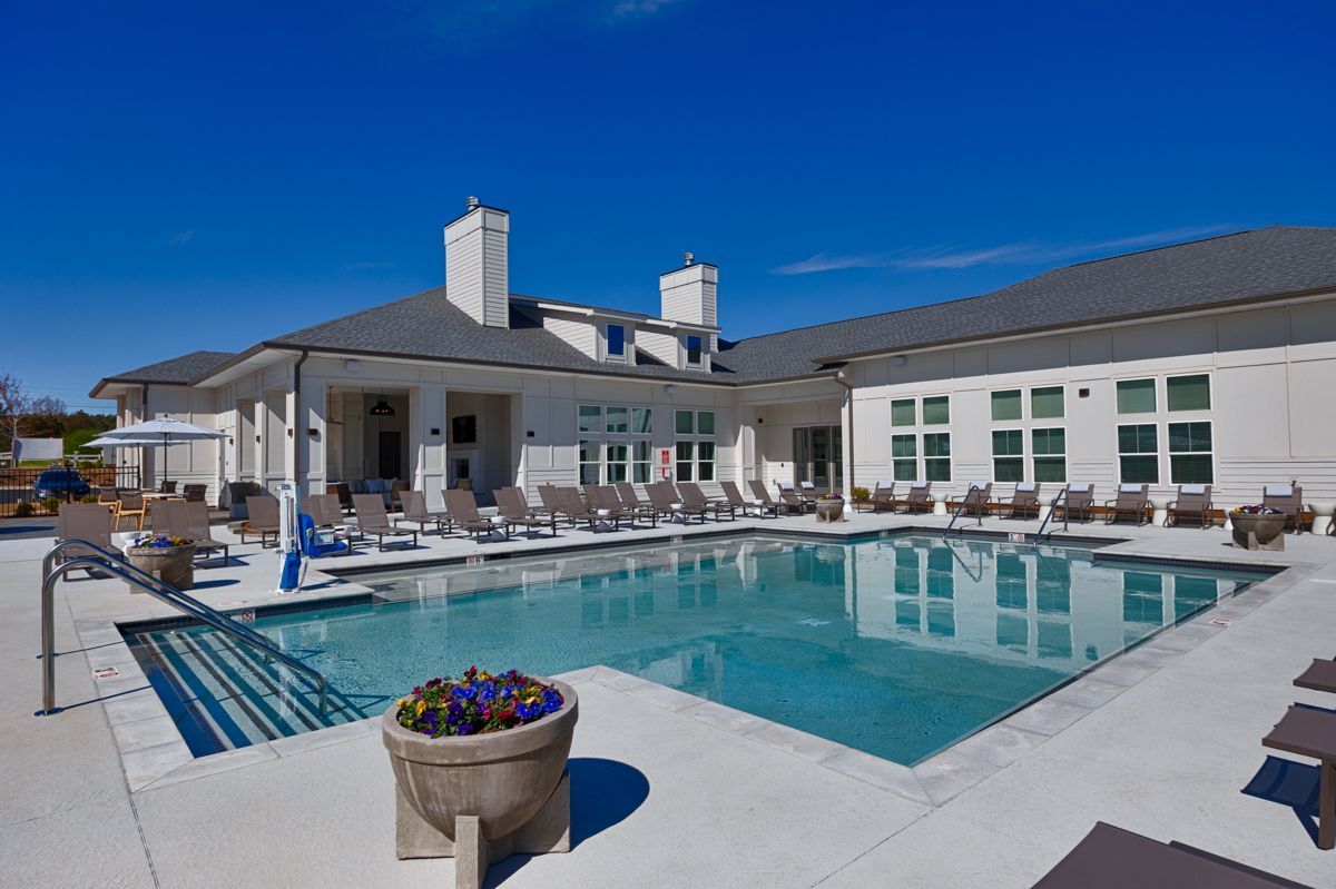 Swimming pool in front of a white building with lounge chairs. Sunny, blue sky overhead.
