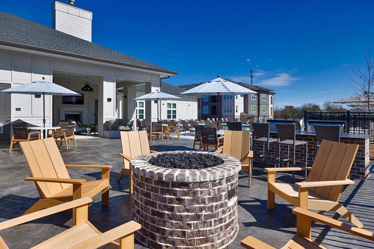 Patio with fire pit and lounge chairs near a building with umbrellas on a sunny day.