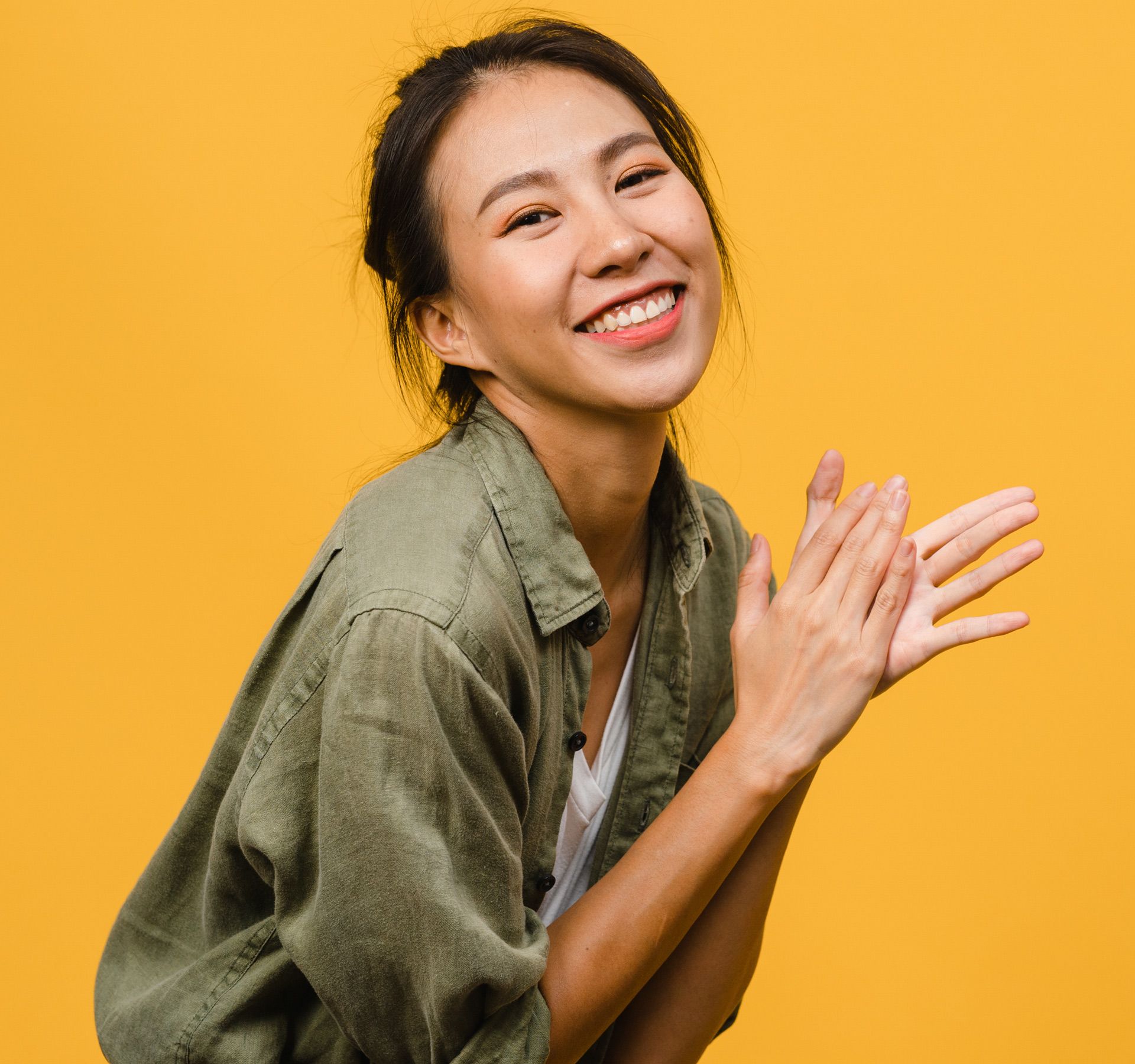 Smiling woman in an olive jacket clapping against a bright yellow background
