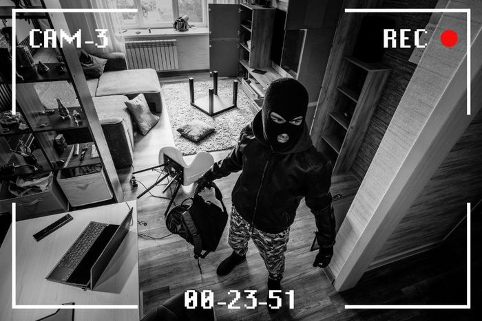 Intruso mascherato in un soggiorno, ripreso da una telecamera di sicurezza con indicatore REC e data/ora.