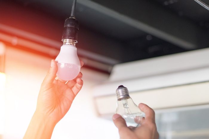 In una stanza luminosa, due mani reggono due lampadine: una brilla di rosa sotto un portalampada sospeso.