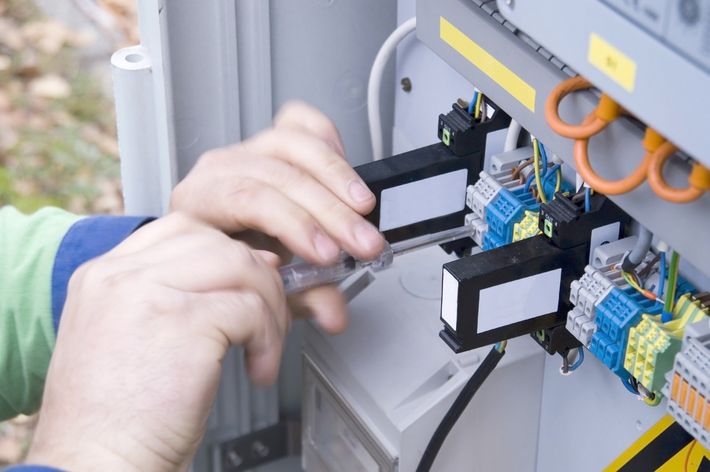 Mani che collegano fili a un quadro elettrico con morsettiere blu e gialle