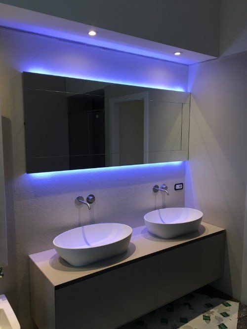 Mobile bagno moderno con due lavabi a ciotola, specchio e illuminazione a LED blu su un piano scuro.