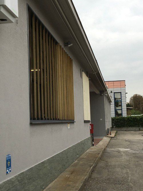 Esterno di un edificio grigio con finestre sbarrate e un angusto passaggio pedonale in cemento accanto.