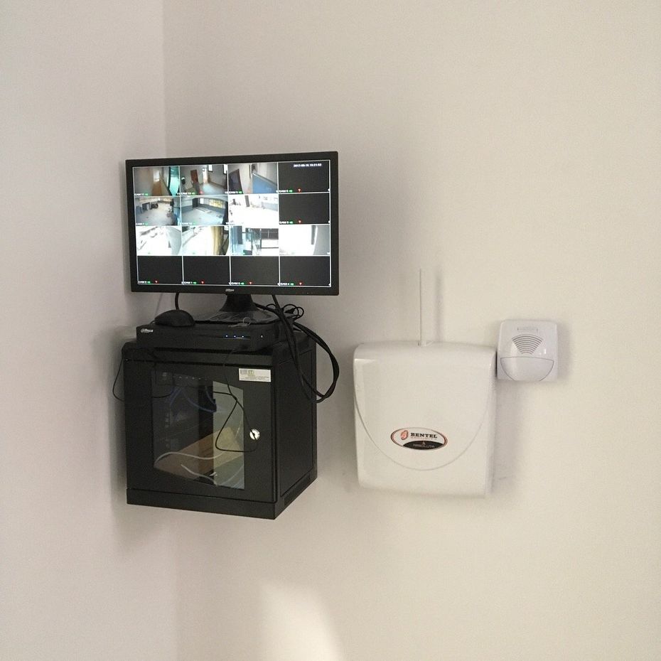 Monitor di videosorveglianza montato a parete sopra un armadietto nero, con dispenser a muro accanto.
