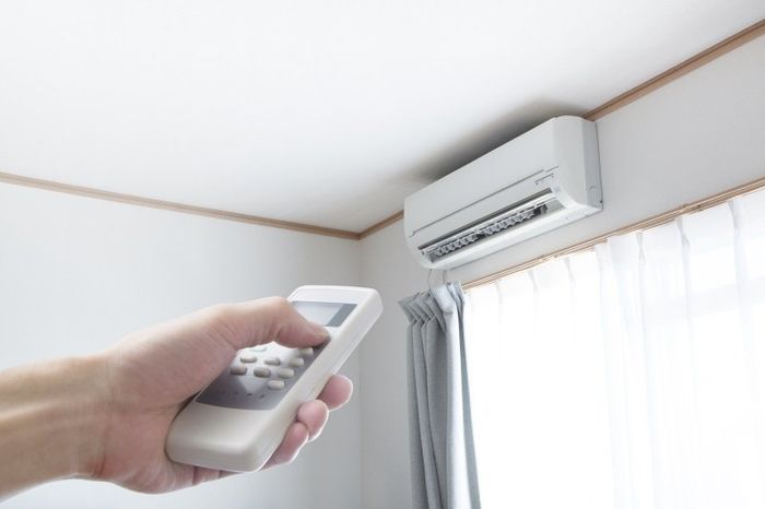 Mano che impugna un telecomando puntato verso un condizionatore d'aria a parete in una stanza luminosa