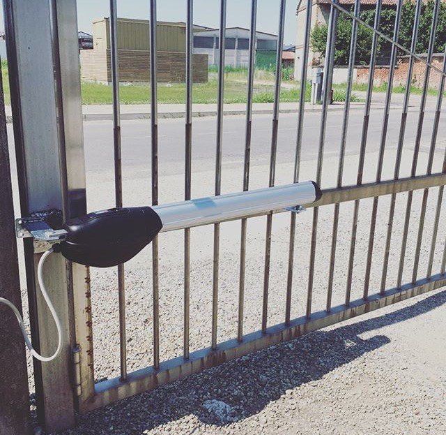 Cancello in metallo con maniglia orizzontale argentata e meccanismo di chiusura nero all'ingresso del vialetto.