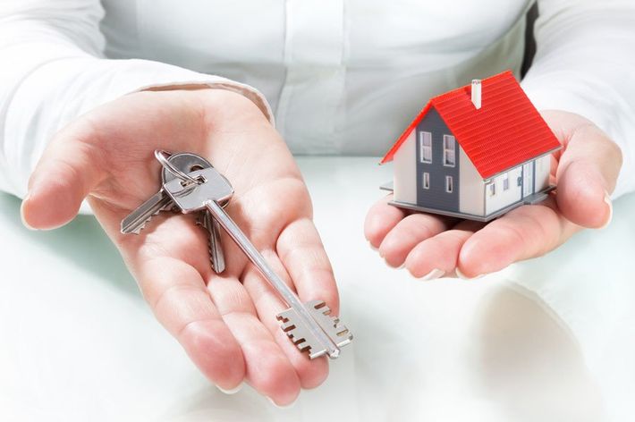 Mani che reggono le chiavi di casa e una piccola casetta in miniatura con il tetto rosso su sfondo bianco.
