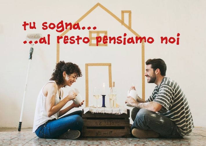 Coppia seduta sul pavimento con tavolino, accanto a testo rosso “Tu sogna… al resto pensiamo noi”.