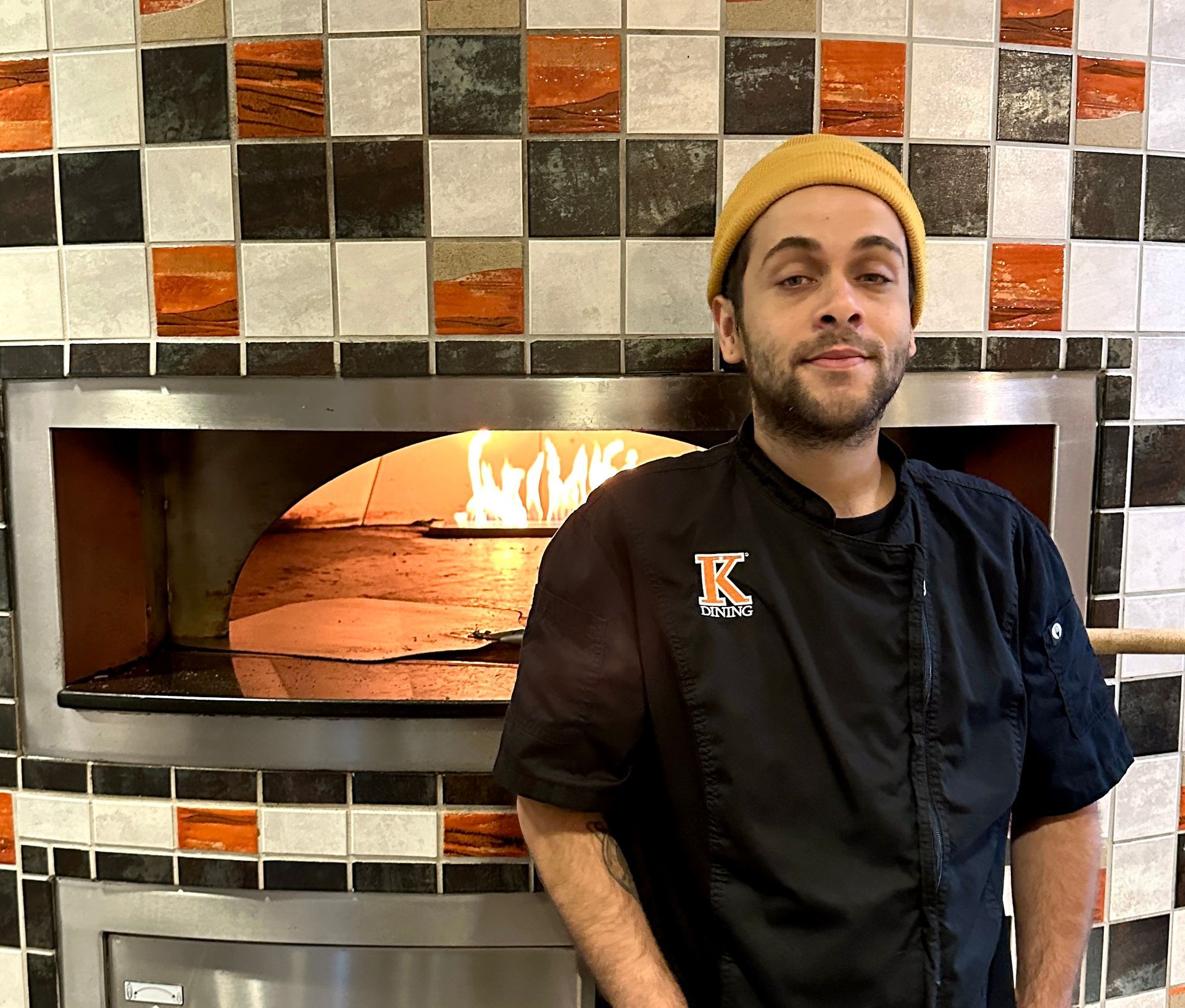 Employee posing in front of a brick pizza oven.