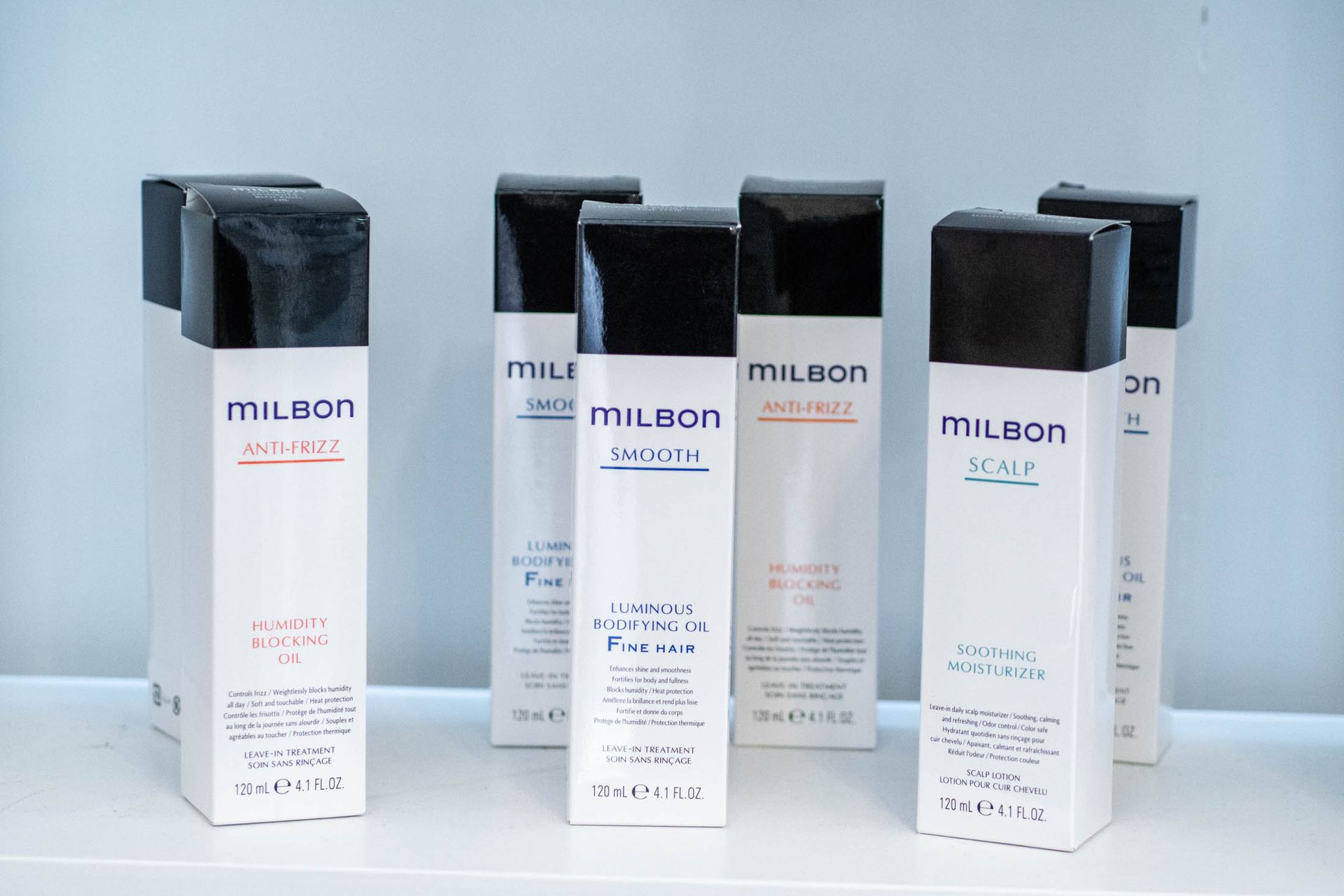 Six white, rectangular Milbon brand hair product bottles with black caps standing on a white surface.