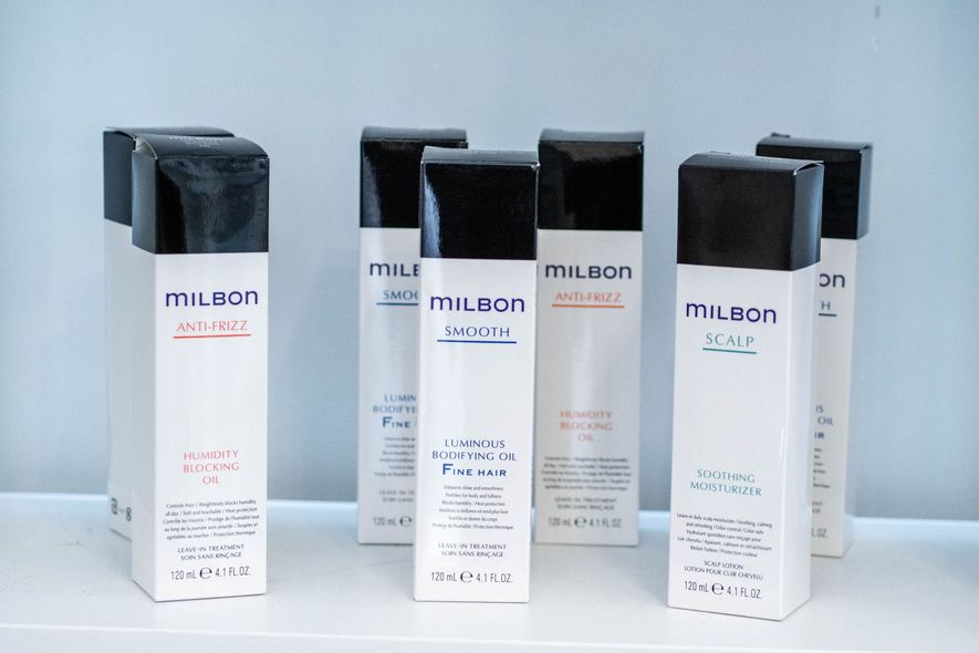 Six white, rectangular Milbon brand hair product bottles with black caps standing on a white surface.