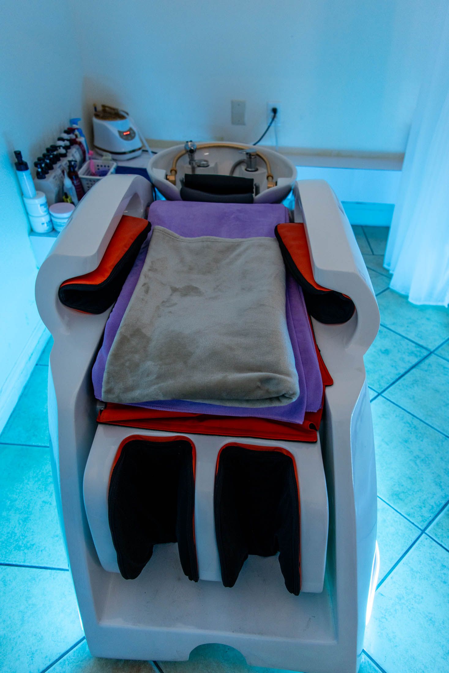 A salon shampoo station with a white chair, a beige towel over a purple cloth, and red accents, set on a tiled floor.