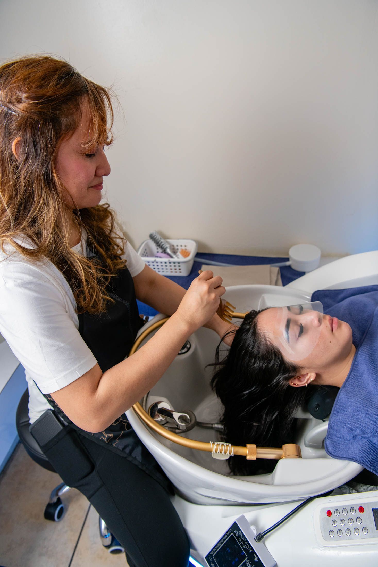 A professional hairstylist washes a client’s hair at a sink in a salon setting.