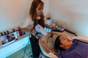 A stylist uses a handheld spray device on a client's hair while the client reclines in a salon sink.