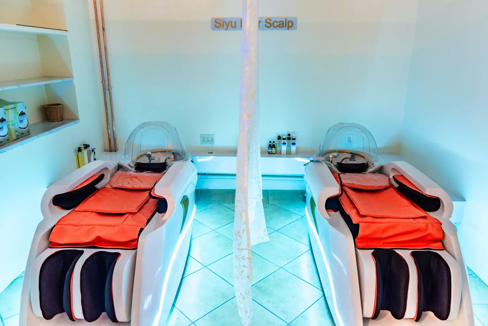 Two white shampoo stations with bright orange bedding and head-covering basins in a minimalist, light-filled salon.