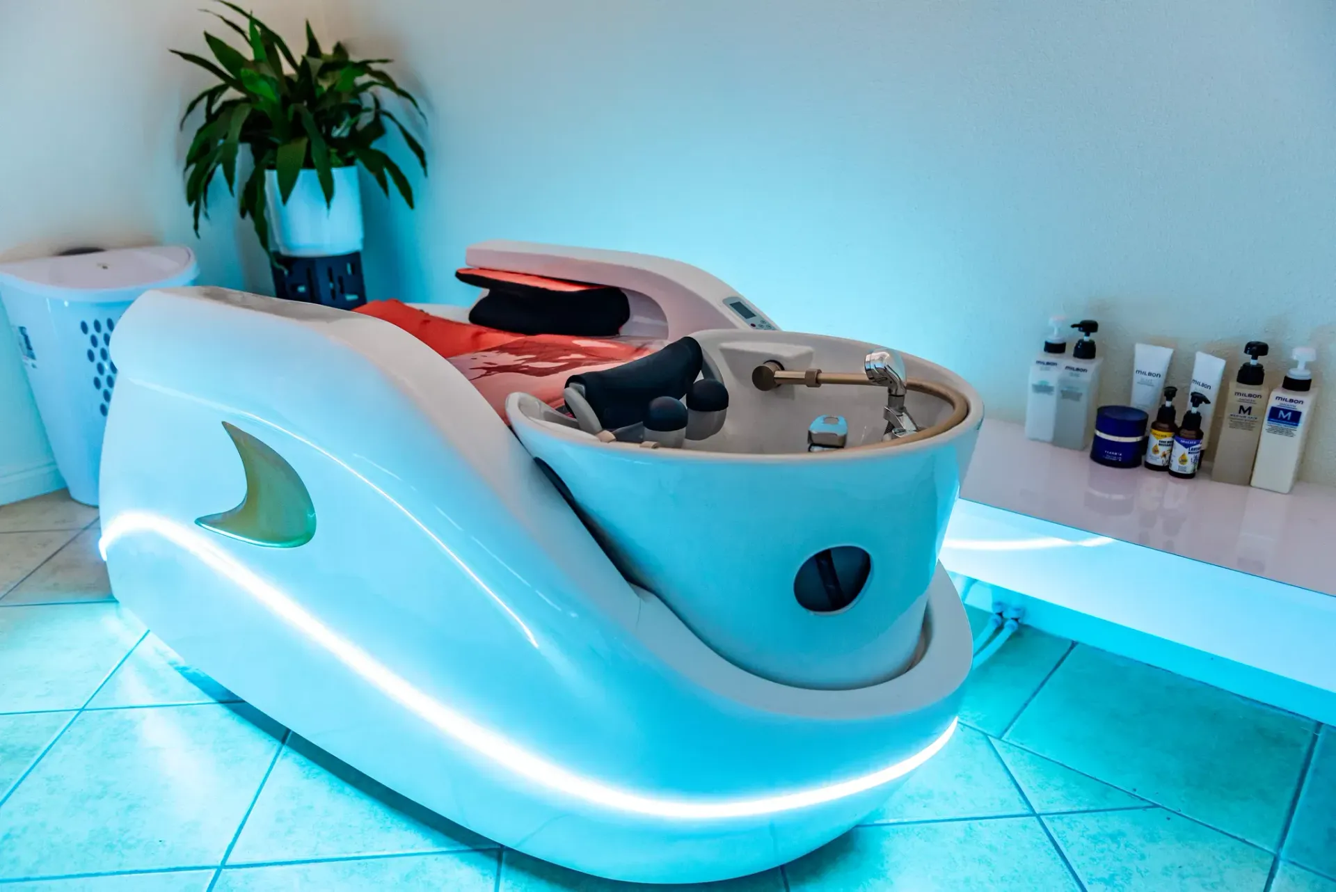 A sleek, white shampoo station with internal blue lighting in a spa, featuring a sink area and various salon products.