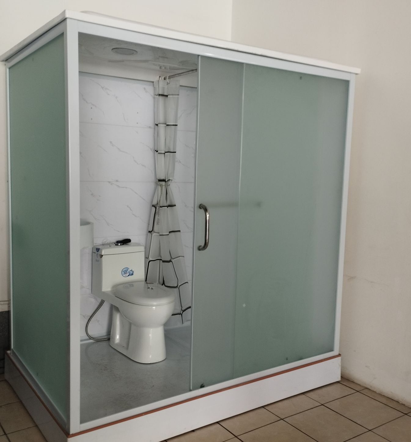 Una pequeña cabina de baño blanca con paredes de cristal, con inodoro y cortina de ducha en el interior.