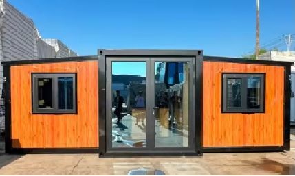 Edificio modular con estructura negra, revestimiento con aspecto de madera y puertas y ventanas de cristal,