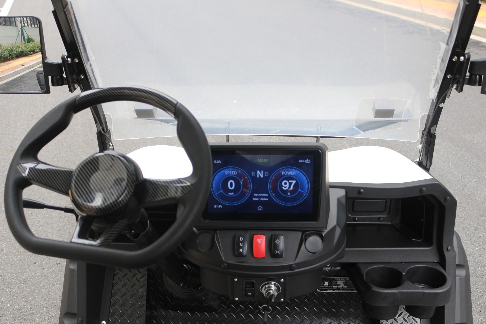 Tablero de un carrito de golf con pantalla digital que muestra la velocidad. Se ven el volante y los portavasos.