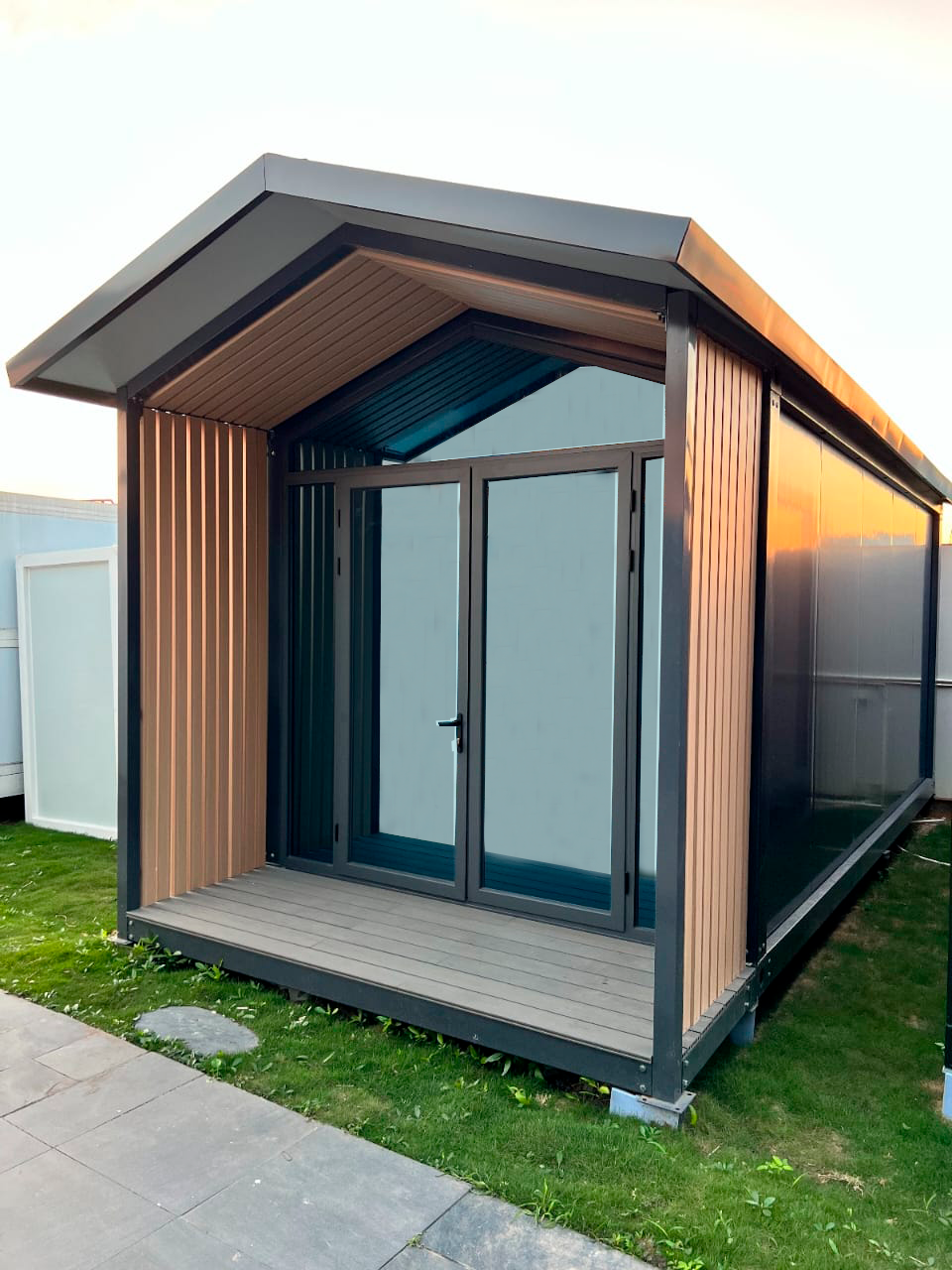 Pequeña y moderna cabaña con techo a dos aguas y grandes puertas de cristal en un césped.