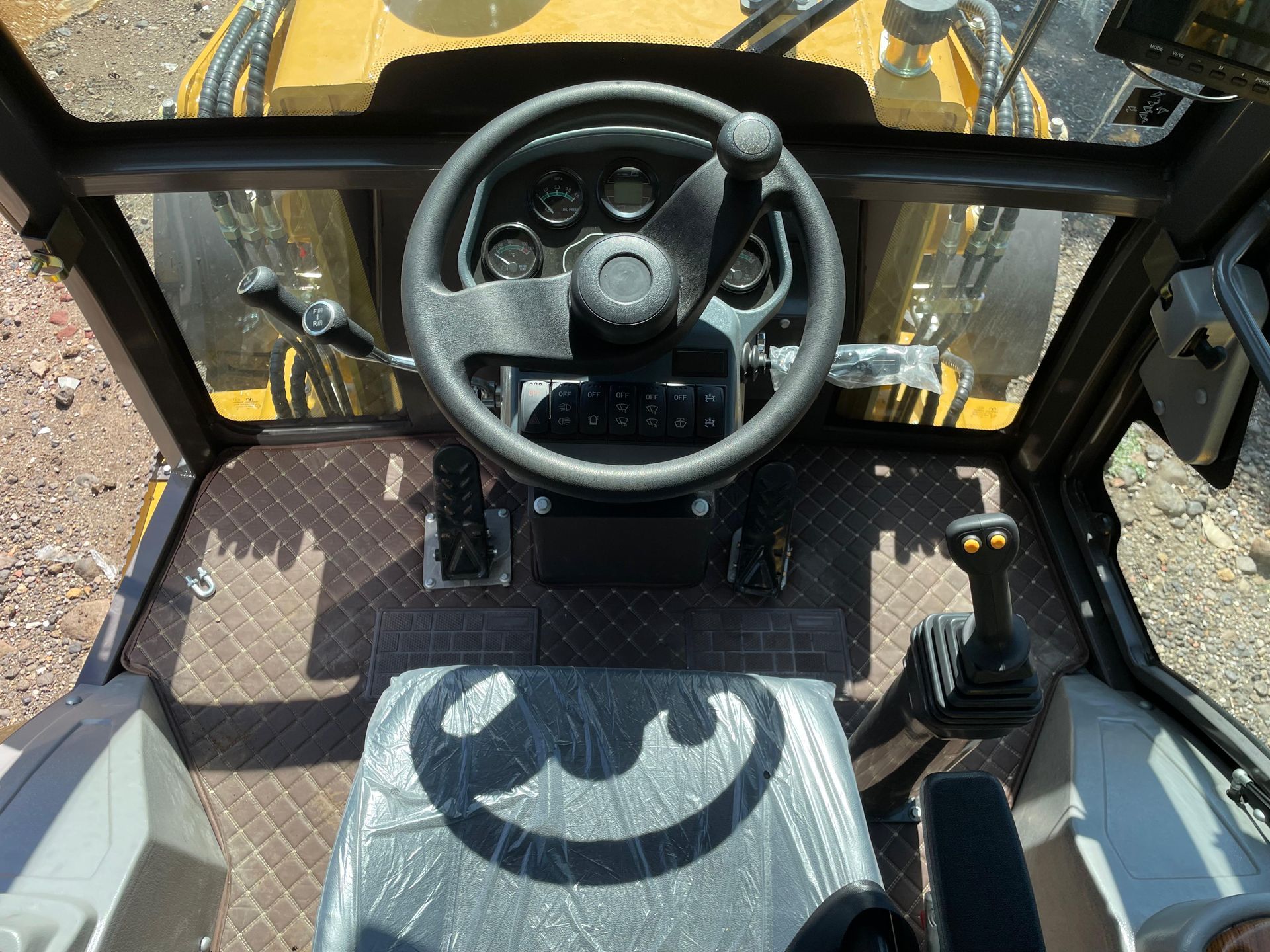Dentro de la cabina de un vehículo de construcción amarillo, se ven un volante, indicadores y controles negros.