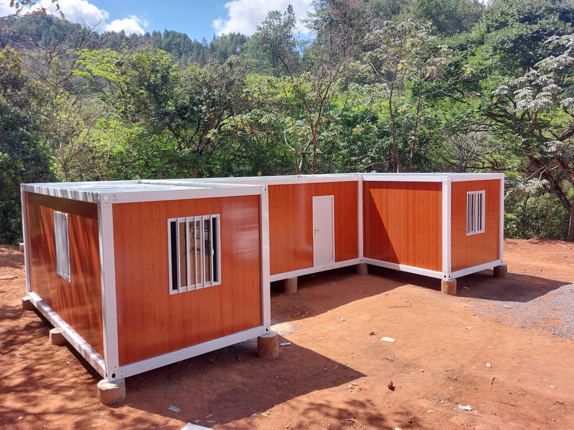 Edificios modulares naranjas con detalles blancos, colocados sobre bloques, en una zona boscosa.
