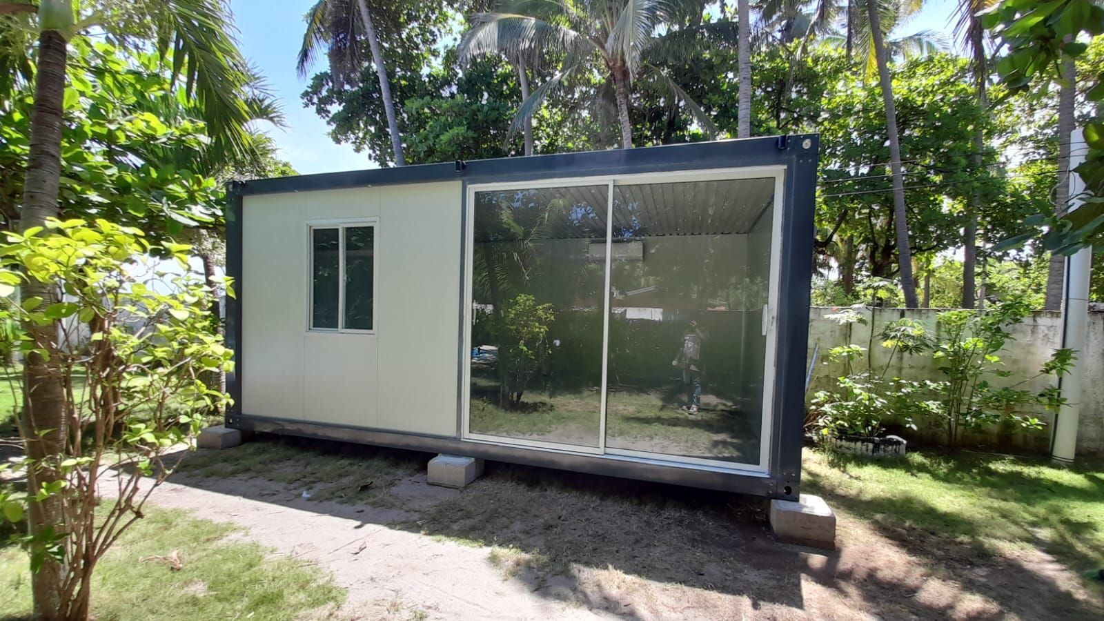 Una casa contenedor rectangular, de color claro, con grandes puertas corredizas de vidrio y una pequeña ventana