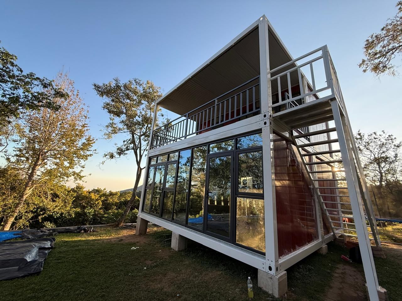 Cabaña moderna de dos plantas con paredes de cristal y escalera metálica en una ladera