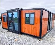 Vivienda modular de contenedores marrones y negros sobre una superficie de grava con puertas y ventanas de cristal.