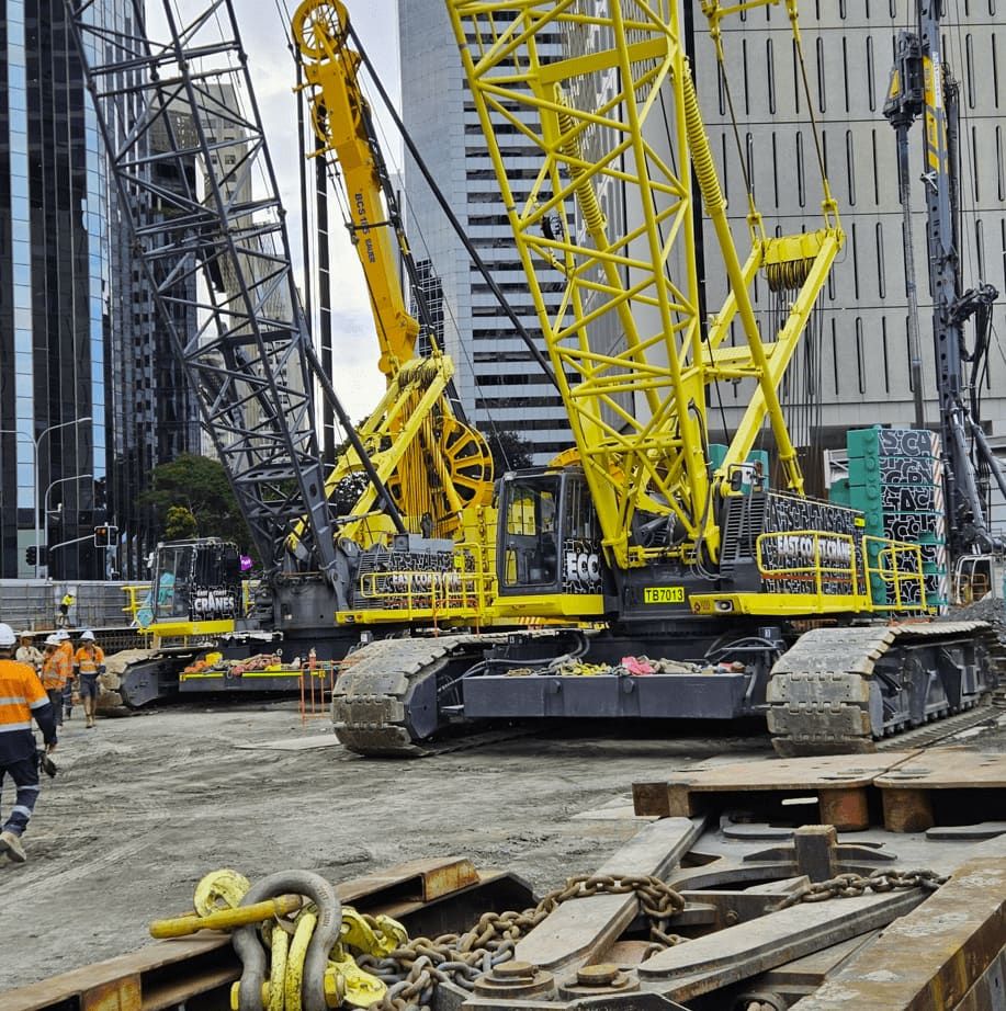 Yellow Construction Cranes on a Work Site With City Buildings in the Background and Workers in Orange Vests — East Coast Cranes in Cairns, QLD