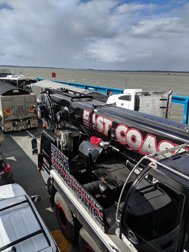 A Black East Coast Crane Truck on a Ferry With Other Vehicles and a Cloudy Sky — East Coast Cranes in Ormeau, QLD