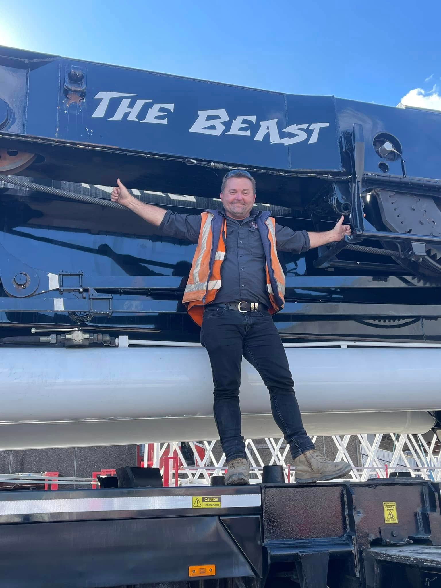 Man in Safety Vest Stands on Crane, Arms Raised — East Coast Cranes in Ormeau, QLD
