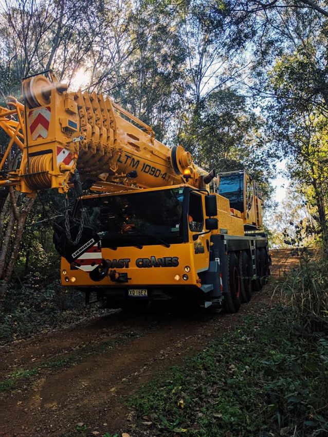 A Yellow Crane is Driving Down a Dirt Road in the Woods — East Coast Cranes in Port Macquarie, NSW