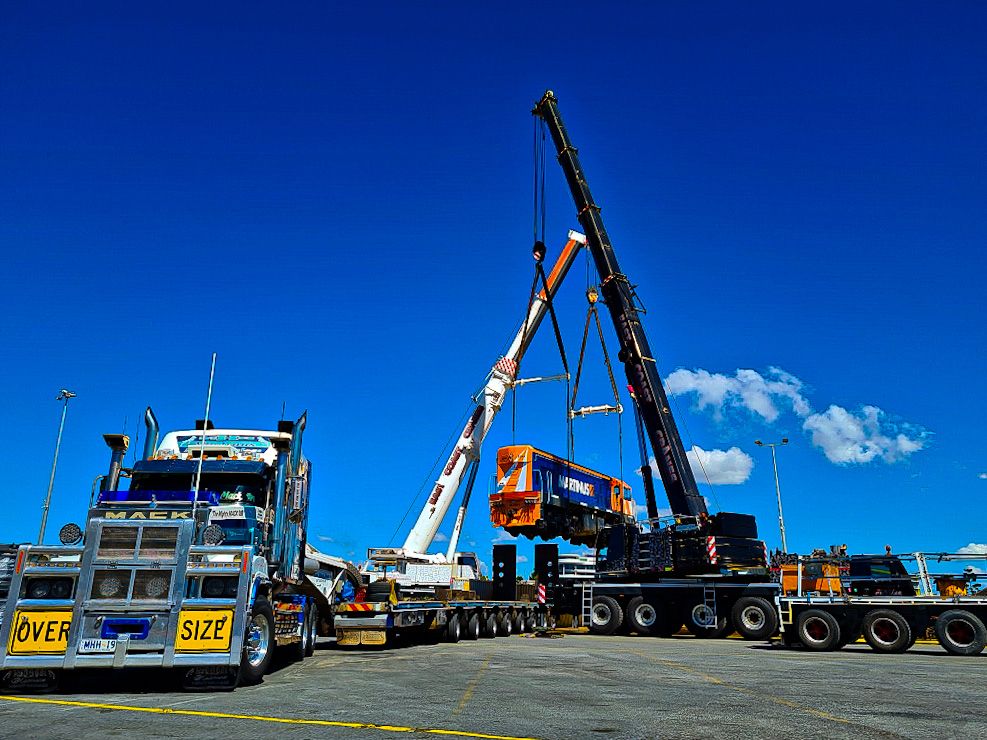 Two Large Cranes Lift a Train Car Onto a Flatbed Truck Under a Blue Sky — East Coast Cranes in Ormeau, QLD
