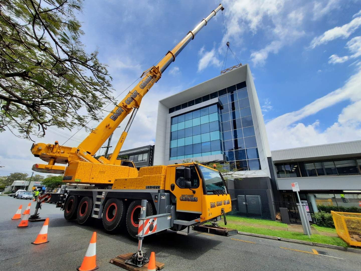 Yellow Crane Lifting Near a Modern Building on a Street With Cones — East Coast Cranes in Ormeau, QLD