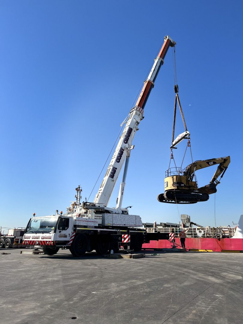 A Large White Crane Lifts an Excavator Against a Blue Sky at a Construction Site — East Coast Cranes in Port Macquarie, NSW