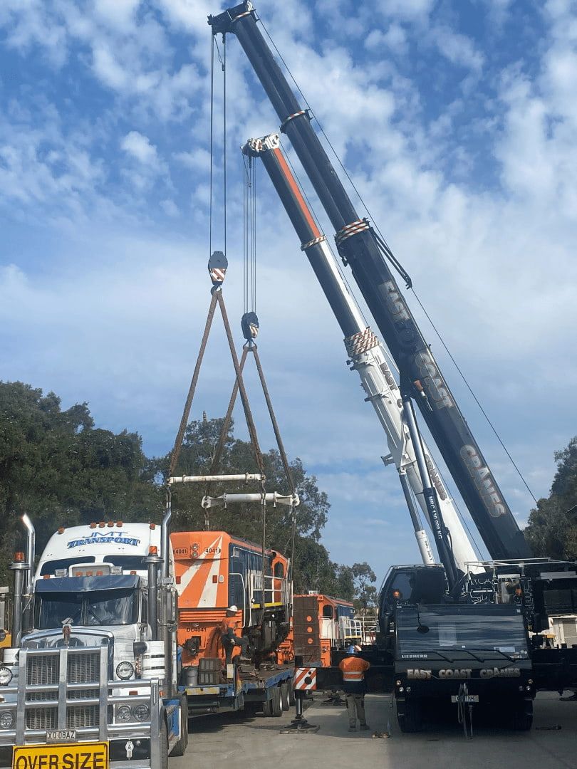 Two Cranes Lifting a Large Object Onto a Truck, Under a Partly Cloudy Sky. Construction Site — East Coast Cranes in Rockhampton, QLD